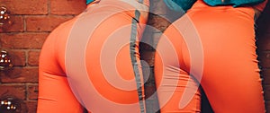 Booty girl in a orange sportswear on a dark background close-up.