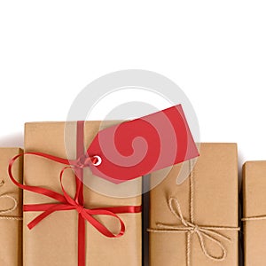 Border of brown paper parcels, one unique with red ribbon bow and gift tag or label, isolated on white background