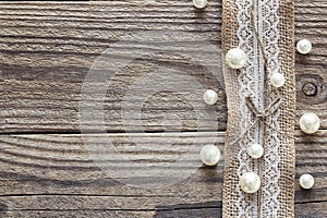 Border of burlap with white lace and beads on old wooden table.