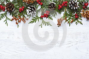 Border of Christmas tree branches pine cones flowers and red berries on white wooden background, copy space