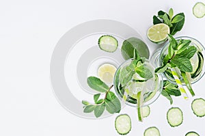 Border of cold drink with ice cubes, slices lime, cucumber, straw, twigs mint with copy space on white wood board, top view.