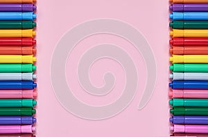 Border of colored felt tip pens on pink background with place for text. Top view