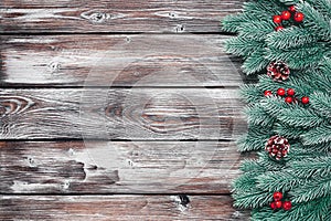 A border of decorative spruce branches with holly and a pine cone on a dark wooden plank background. Christmas