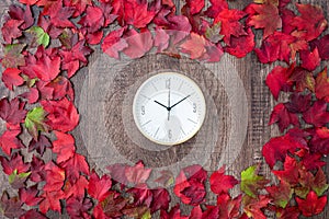 Border of fall color in red, green, yellow, and orange maple leaves on a rustic wood background, with round white analog clock