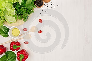 Border of fresh green greens, red paprika, cherry tomato, pepper, oil and utensils on soft white wooden background.