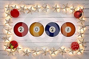 A border of golden star christmas lights, and red baubles, with 2021 written oon pool balls on a destressed woodern background