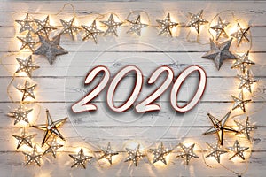 A border of golden star christmas lights, and star baubles, with 2020 in the middle, on  destressed wood