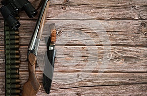 The border is made of hunting weapons, bandolier with cartridges, binoculars and a knife in a case on a wooden background.