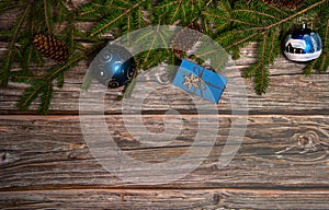 The border is made of spruce branches, cones, gift box and blue Christmas balls on a wooden background. Christmas, winter, New yea