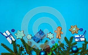 The border is made of spruce branches, cones, gift boxes, glazed homemade gingerbread, blue balls and serpentine on a blue backgr