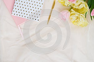 A border of pink flowers of yellow tulips, accessories and cosmetics on the background. Women`s home office desk layout. Flat lay