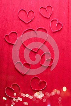 Border from pink paper hearts on red textured paper surface.