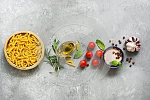 Border raw pasta and ingredients for cooking. Fusilli, tomatoes, basil, olive oil, himalayan salt, peppercorns, rosemary and