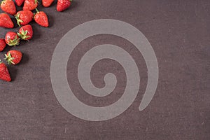 Border of whole fresh ripe red strawberries arranged on left sides on a dark textured slate background with copyspace. Fresh berry