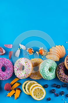 Bordure of colorful fresh donuts with different kinds of topping and fruits on blue paper background.