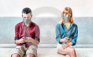 Bored addicted couple with protective masks using tracking app with mobile smartphones - Young millenial man and woman sharing