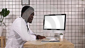 Bored african doctor waiting for something by the computer screen. White Display.