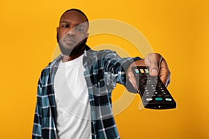 Bored African Man Switching Channels Pointing Television Controller, Yellow Background