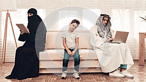 Bored Arabian Boy Sitting with Family on Sofa.