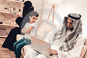 Bored Arabian Boy Sitting with Family on Sofa.