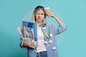 Bored Asian female office worker with a lot of work with holding document file with cup of coffee and note on face standing on