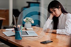 Bored asian female worker lie at office desk look at mobile phone and laptop screen think about problem solution, tired