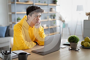 Bored Asian male student sitting at desk with pc