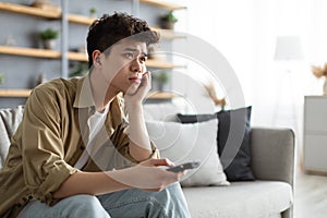 Bored asian man watching television sitting on couch