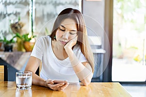 Bored asian woman looking disappointed at her smart phone while waiting someone