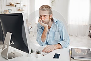 Bored bearded Caucasian office worker with desperate look facing deadline but failing to finish report in time, looking