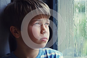 Bored of being bored. Shot of a sad young boy watching the rain through a window at home.