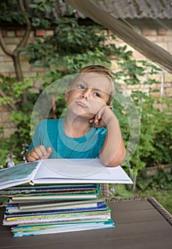 Bored boy 5-6 years old sitting at a table in front of a stack of books