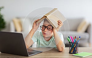 Bored boy doing homework in front of laptop at home