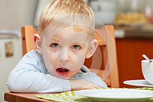 Bored boy waiting for breakfast, sitting in ktichen