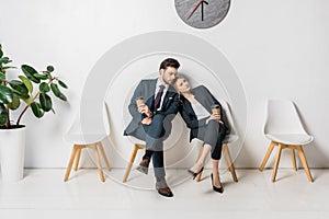 bored business colleagues with paper cups sitting on chairs