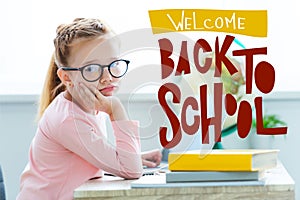 Bored child in eyeglasses looking at camera while studying with laptop and books with welcome back to