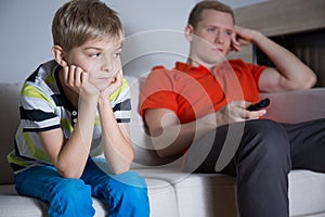 Bored child with his father sitting and watching tv photo