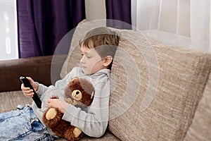 Bored child sitting on the sofa and watching tv.