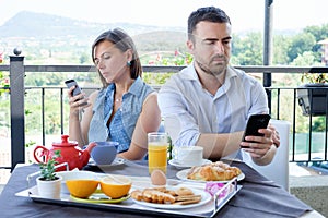 Bored couple using smartphone during breakfast