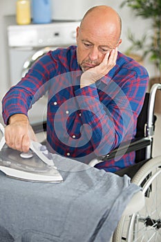 Bored disabled man on wheelchair ironing clothing