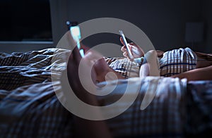 Bored distant couple ignoring each other lying in bed at night while using mobile phones. Smartphone addict.