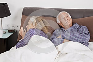 Bored elderly man looking away while spouse sleeping besides in bedroom