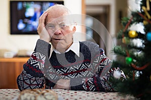 Bored elderly man sitting alone at home table at Christmas