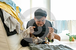 Bored face Asian man picking up and arranged clothes. Concept of housework.