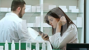Bored female pharmacist use mobile phone at pharmacy