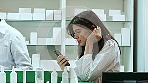 Bored female pharmacist use mobile phone at pharmacy