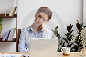 Bored female sitting at desk looking at laptop screen