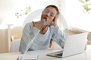 Bored female sitting at workplace feels sleepy putting head in her hand