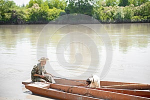 Bored fisherman going fishing with pet, while sitting in rowing old boat at shore in morning.