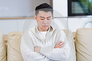 Young asian man sitting on sofa at home alone. Misses male sitting on the couch in apartment. Lonely guy indoors